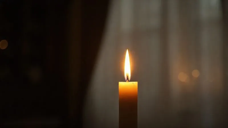 A single, glowing candle in a dimly lit, serene room, symbolizing remembrance and hope for justice, with a soft blur in the background. Photorealistic, professional photography, 8K, cinematic lighting, sharp focus, depth of field, shot on a high-end DSLR.