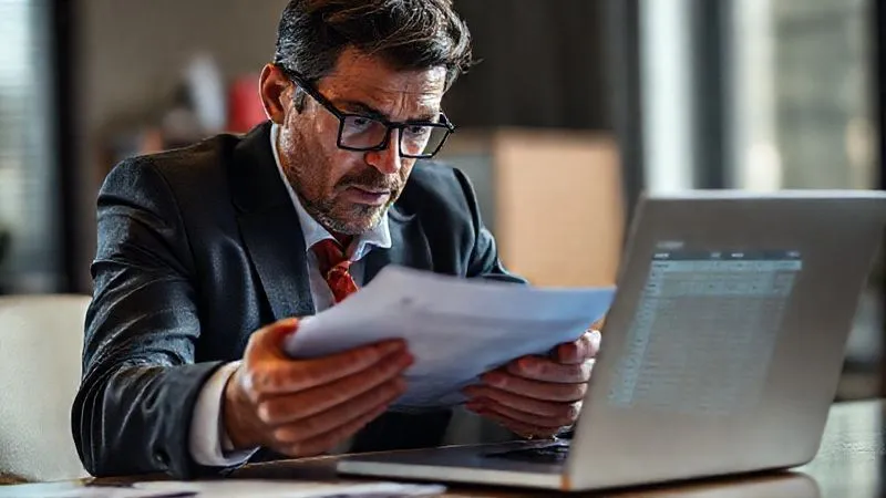 A photorealistic, professional photography, 8K, cinematic lighting, sharp focus, depth of field, shot on a high-end DSLR, of a sports lawyer intently reviewing a stack of documents, with a laptop displaying ADAMS logs open beside them, symbolizing thorough evidence gathering. The lawyer's face shows concentration and determination.