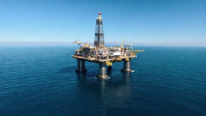 A photorealistic architectural rendering of a massive, fixed offshore oil platform on the Outer Continental Shelf, surrounded by calm, deep blue water under a clear sky. The platform is intricately detailed, showing helipad, living quarters, and drilling equipment. Professional photography, 8K, cinematic lighting, sharp focus on the platform, depth of field blurring the distant horizon, conveying scale and isolation.